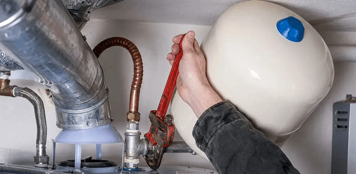 Water heater repair technician tightening plumbing connections near a tank unit in Tuscaloosa, AL